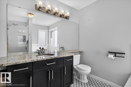 Modern bathroom featuring a granite-look countertop, dark wood-finish vanity with ample storage, and a large wall-mounted mirror - 13 Baie Madelene, Beaumont, AB 