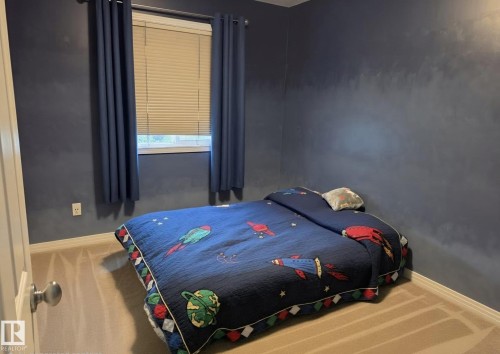 Carpeted room featuring a single window with blinds and dark blue drapery - 13 Baie Madelene, Beaumont, AB 