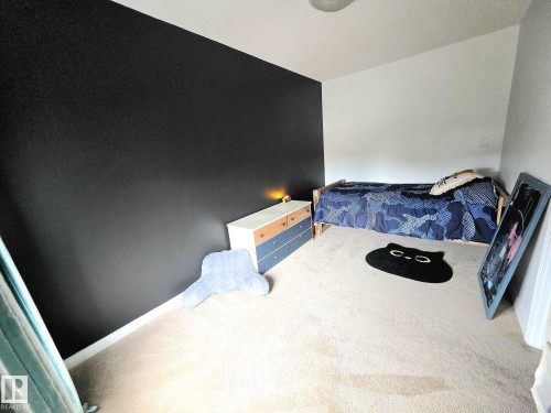 Room featuring a dark accent wall, light-colored carpeting, a ceiling-mounted light fixture, and white baseboards - 13 Baie Madelene, Beaumont, AB 