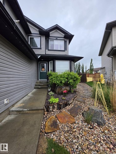 Two-story residence featuring light gray siding with dark trim, a dark green entry door, and a bay window - 13 Baie Madelene, Beaumont, AB 
