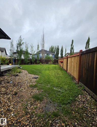 Expansive backyard featuring a manicured lawn, a two-tone wooden privacy fence, and a decorative rock border - 13 Baie Madelene, Beaumont, AB 