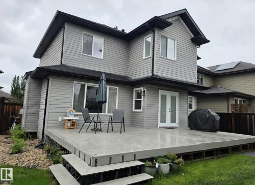 Rear exterior featuring light grey siding with dark trim, a multi-level composite deck, and double French doors - 13 Baie Madelene, Beaumont, AB 