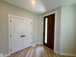 Entryway with wood-finish flooring, a contemporary dark wood entry door with vertical glass insert, white interior doors with black hardware, and recessed ceiling lighting - 