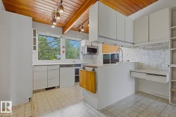 Kitchen featuring a wood-panel ceiling with exposed beams, white cabinetry, a tiled backsplash, built-in shelving, and light-colored tile flooring - 
