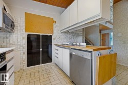 Kitchen featuring a wood-panel ceiling, white upper cabinetry, mosaic tile backsplash, a stainless steel dishwasher, and a wood-finish countertop with an integrated sink - 