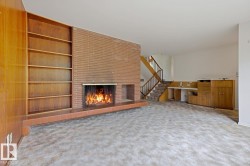 Brick fireplace with a tiled hearth and a wood-paneled wall featuring built-in shelving - 