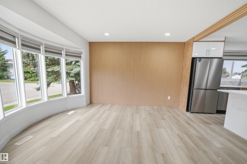 Open concept living area featuring a curved bay window, light wood-finish flooring, and a contemporary slatted wood accent wall - 3548 20 Ave, Edmonton, AB 