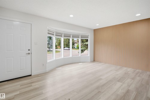 Spacious room featuring light wood-finish flooring, a prominent bay window, recessed lighting, and a slatted accent wall - 3548 20 Ave, Edmonton, AB 