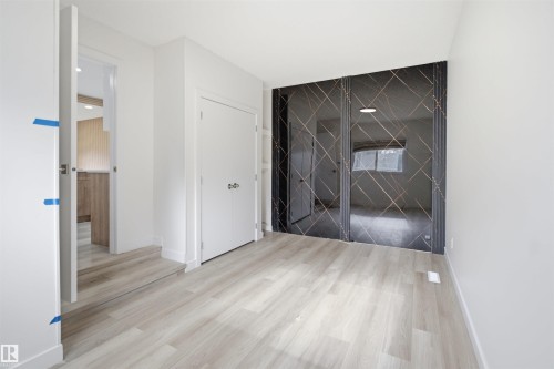 Contemporary interior with light wood-finish flooring, white walls, and a striking dark accent wall featuring geometric detailing - 3548 20 Ave, Edmonton, AB 