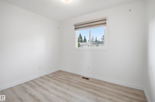 Bright interior space featuring a window with integrated blinds, wood-finish flooring, white baseboards, and a ceiling-mounted light fixture - 3548 20 Ave, Edmonton, AB 