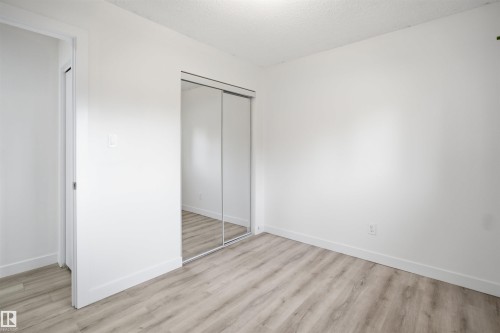 Room featuring wood-finish flooring, white baseboards, and a mirrored sliding closet door - 3548 20 Ave, Edmonton, AB 