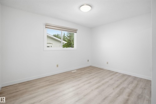 Room featuring wood-finish flooring, white baseboards, a single window with a roller shade, and a flush-mount ceiling light - 3548 20 Ave, Edmonton, AB 