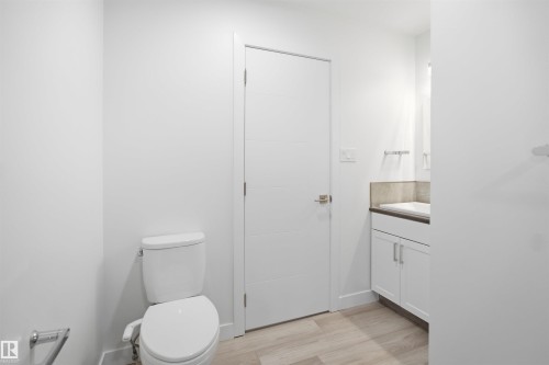 Contemporary bathroom featuring light wood-finish flooring, a white vanity with a dark countertop, a rectangular undermount sink, and a modern white paneled door - 3548 20 Ave, Edmonton, AB 