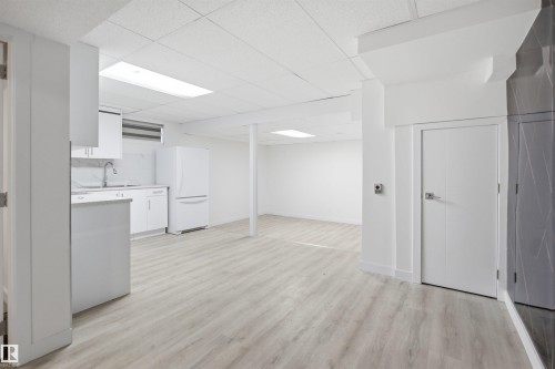 Open-concept interior featuring light wood-finish flooring and a kitchen area with white cabinetry, a double-basin sink, and a white refrigerator - 3548 20 Ave, Edmonton, AB 
