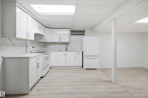 2nd Kitchen space featuring white cabinetry with silver-tone hardware, a white electric range, a white refrigerator, and a stainless steel sink with a chrome faucet - 3548 20 Ave, Edmonton, AB 