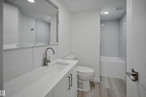 Modern bathroom featuring a contemporary vanity with an integrated sink and brushed nickel faucet, a spacious mirror, and a full-size bathtub with tiled surround - 3548 20 Ave, Edmonton, AB 