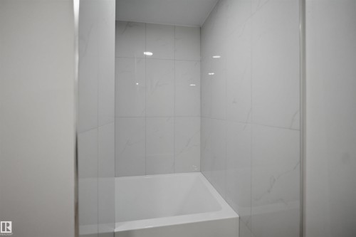 Recessed bathtub with white rectangular basin, framed by large format marble-look wall tiling and a partial glass shower enclosure - 3548 20 Ave, Edmonton, AB 