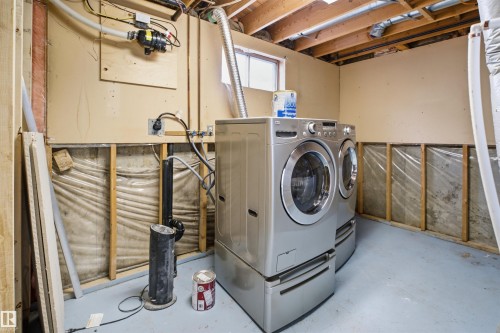 Dedicated laundry area featuring a front-loading washer and dryer set, exposed ceiling joists, and a small window - 3548 20 Ave, Edmonton, AB 