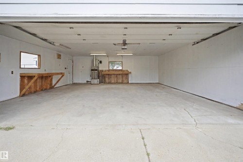 Over sized Double car garage with gas heater- Spacious garage interior featuring a concrete floor, built-in wooden workbenches, and overhead fluorescent lighting - 3548 20 Ave, Edmonton, AB 