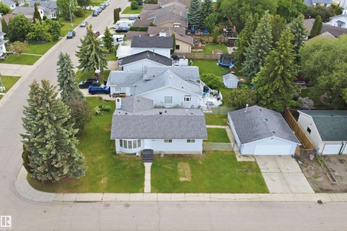 Corner lot residence featuring a well-maintained lawn, mature evergreen trees, and a detached garage - 3548 20 Ave, Edmonton, AB 