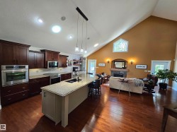 Open-concept kitchen and living area featuring wood-finish flooring, vaulted ceilings, and recessed lighting - 