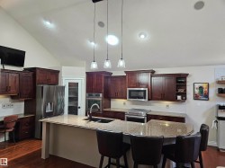 Gourmet kitchen featuring dark wood cabinetry, granite countertops, stainless steel appliances, and a central island with pendant lighting - 
