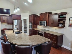 Kitchen featuring dark wood cabinetry, a large U-shaped island with a built-in sink, and light-colored speckled countertops - 