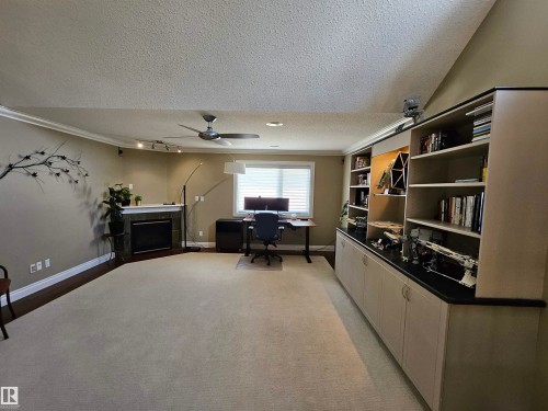 Spacious recreation room featuring extensive built-in cabinetry and shelving, a decorative fireplace with a mantel, a ceiling fan, and track lighting - 2322 Rutherford Way, Edmonton, AB 