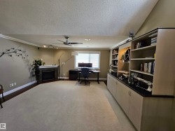 Spacious recreation room featuring extensive built-in cabinetry and shelving, a decorative fireplace with a mantel, a ceiling fan, and track lighting - 