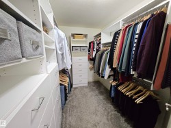 Custom closet system featuring multiple hanging rods, integrated shelving, built-in drawers with modern hardware, and soft gray carpeting - 