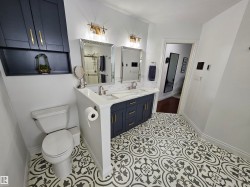 Dual vanity featuring undermount sinks, stone countertops, and dark blue cabinetry with gold-tone hardware - 