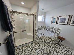 Bathroom featuring patterned tile flooring and tub surround, a corner soaking tub with deck-mounted fixtures, and a glass-enclosed shower with a built-in seat - 