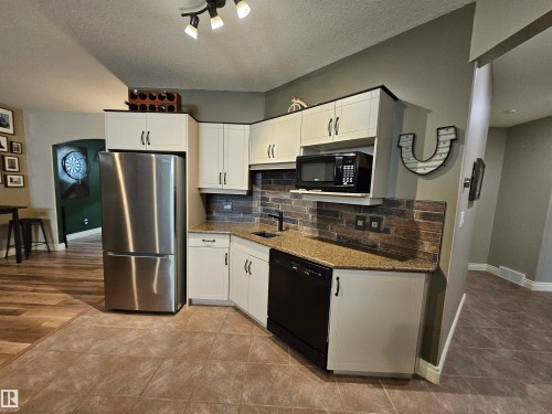 Compact kitchen area featuring light cabinetry, a stainless steel refrigerator, and a dark tile backsplash - 2322 Rutherford Way, Edmonton, AB 