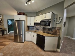 Compact kitchen area featuring light cabinetry, a stainless steel refrigerator, and a dark tile backsplash - 