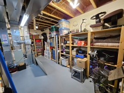 Unfinished basement space with exposed ceiling joists and ductwork, featuring a painted concrete floor and fluorescent overhead lighting - 