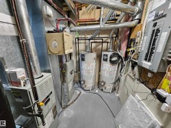 Utility area featuring two water heaters, two furnaces, and multiple electrical panels - 