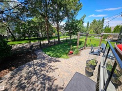 Paved patio with decorative string lighting, surrounded by mature trees, a manicured lawn, and black chain-link fencing - 