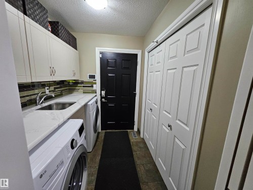 Utility area featuring a stainless steel sink, quartz-finish countertop, white cabinetry with brushed nickel hardware, and tile flooring - 2322 Rutherford Way, Edmonton, AB 