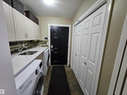 Utility area featuring a stainless steel sink, quartz-finish countertop, white cabinetry with brushed nickel hardware, and tile flooring - 