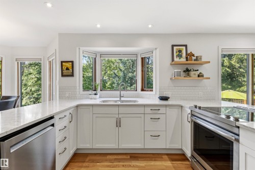 Bright kitchen featuring a bay window, white cabinetry, a stainless steel sink with a gooseneck faucet, light-toned countertops, and wood-finish flooring - 624 Butchart Wynd, Edmonton, AB 