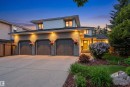 Contemporary two-story residence featuring a triple attached garage with individual doors, brick and siding exterior, illuminated entryway, mature landscaping, and a concrete driveway - 624 Butchart Wynd, Edmonton, AB 