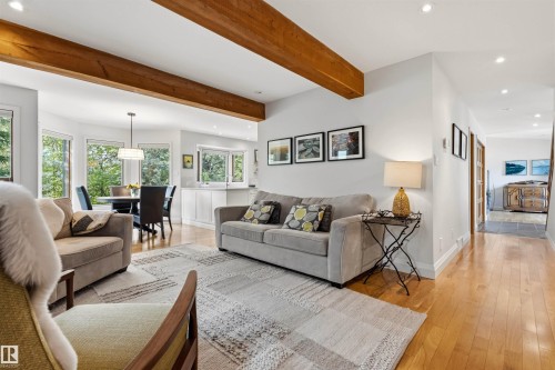 Open-concept living space featuring wood-finish flooring, exposed ceiling beams, recessed lighting, and a dining area with expansive windows - 624 Butchart Wynd, Edmonton, AB 