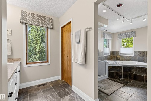 Spacious bathroom featuring stone-look tile flooring, a white vanity with a light-colored countertop, and a window with a patterned valance - 624 Butchart Wynd, Edmonton, AB 