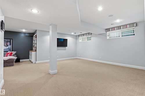 Expansive carpeted room featuring recessed lighting, a built-in cabinetry unit with shelving, light gray walls, and two horizontal windows with valances - 624 Butchart Wynd, Edmonton, AB 