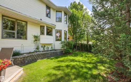 Manicured lawn with mature trees, stone retaining wall, and a raised wood-finish deck - 624 Butchart Wynd, Edmonton, AB 