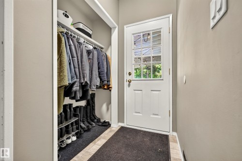 Entryway featuring a white paneled door with divided lite glass, tiled flooring, and a built-in closet with shelving and a hanging rod - 24 Addison Crescent, St. Albert, AB 