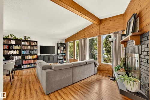 Living area featuring wood-finish flooring, wood-paneled walls, a brick-faced fireplace with a metal insert, and multiple windows - 24 Addison Crescent, St. Albert, AB 