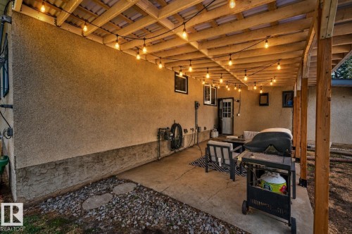Expansive covered patio featuring a concrete floor, exposed wood beam ceiling, and string lighting - 24 Addison Crescent, St. Albert, AB 
