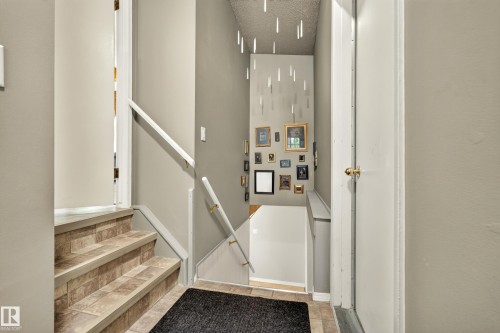 Foyer area featuring staircase with tile-finish treads and risers, white handrail, neutral wall paint, and a white interior door - 24 Addison Crescent, St. Albert, AB 