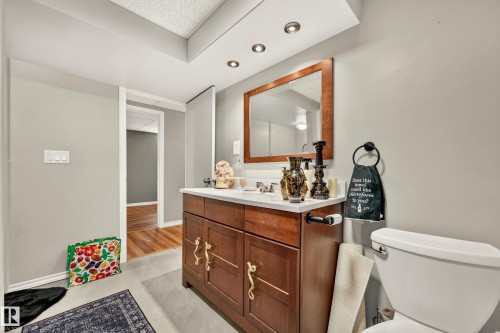 Bathroom featuring a wood-finish vanity with a light-toned countertop, a rectangular mirror with a wood frame, and recessed lighting - 24 Addison Crescent, St. Albert, AB 